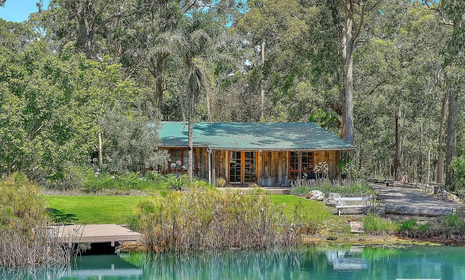 A timber cabin at the edge of the water, seen through bush